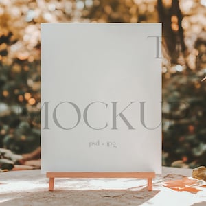 May include: A white sign with the text "MOCKUP psd + jpg" on a wooden easel in a forest setting. The sign is surrounded by green leaves and branches.