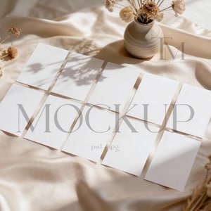 Puede incluir: Una maqueta con tarjetas rectangulares blancas dispuestas sobre una tela de satén beige. La palabra "MOCKUP" está impresa en una fuente gris claro en las tarjetas. También hay flores secas y un pequeño jarrón, creando una estética suave y natural.