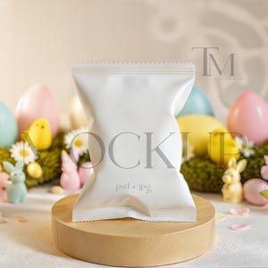 May include: A white product package stands on a wooden round platform, surrounded by Easter decorations. Pastel-colored eggs, flowers, and small figurines of bunnies and chicks are arranged on a bed of green moss, creating a festive scene.