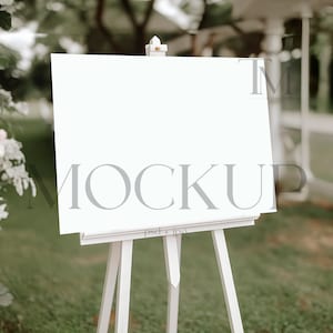 Könnte beinhalten: Ein weißer Staffelei mit einem leeren Schild vor einem weißen Pavillon und grünem Gras. Das Schild ist ein Mockup für eine Hochzeit oder eine Veranstaltung.