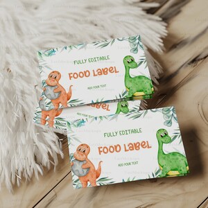 May include: A stack of fully editable food labels with a dinosaur theme. The labels feature illustrations of orange and green dinosaurs, with text that reads "FOOD LABEL" and "ADD YOUR TEXT". The labels are decorated with green foliage.