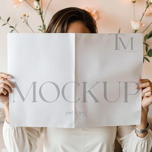 Op de afbeelding: Een wit mockup-vel papier met het woord "MOCKUP" in grijze tekst. Het papier wordt voor het gezicht van een persoon gehouden.