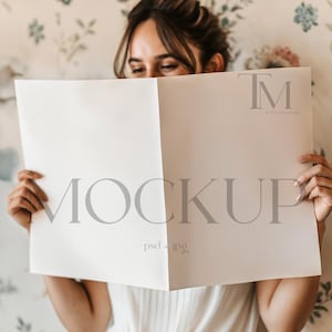 Peut inclure: Une maquette blanche d'un magazine avec le texte "MOCKUP psd + jpg" imprimé sur la face avant. Le magazine est tenu par une personne, dont seules les mains et le haut de la tête sont visibles.