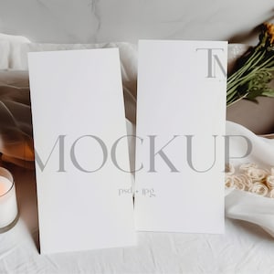 May include: Two blank white cards on a white linen surface with a lit candle, a bowl of dried flowers, and the text "MOCKUP psd + jpg" in gray.