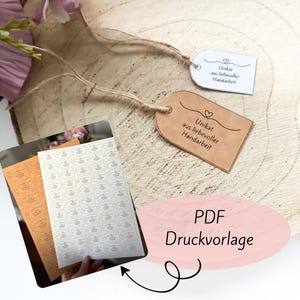 Puede incluir: Una superficie de madera muestra dos etiquetas con el texto "Unikat aus liebevoller Handarbeit" y una hoja de pegatinas. Las etiquetas son marrones y blancas, con un diseño de corazón. Las pegatinas están en hojas de color naranja y blanco. La imagen también incluye el texto "PDF Druckvorlage".