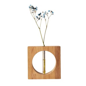 May include: A square wooden vase with a circular cutout, holding a sprig of blue and white flowers. The vase has a natural wood grain finish and a small glass tube inside to hold water for the flowers.