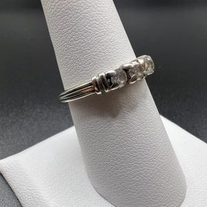 Op de afbeelding: Een zilveren ring met vijf heldere stenen in een rij. De ring ligt op een witte ringstandaard.