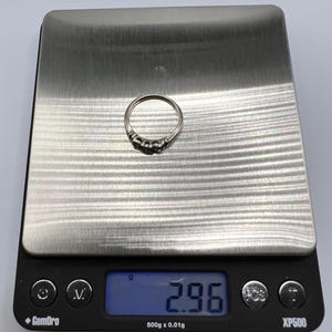 Op de afbeelding: Een zilveren ring met vijf kleine stenen op een digitale weegschaal die 2,96 gram aangeeft.