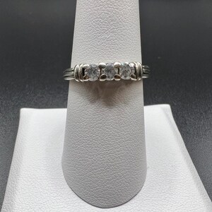 Op de afbeelding: Een zilveren ring met drie ronde, heldere stenen gezet in een band met een textuurontwerp.