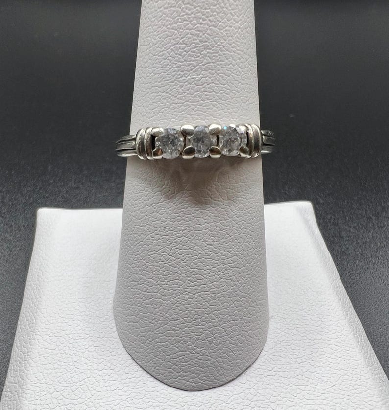Op de afbeelding: Een zilveren ring met drie ronde, heldere stenen gezet in een band met een textuurontwerp.