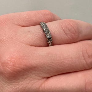 Op de afbeelding: Een zilveren bandring met vijf kleine ronde diamanten in een rij.