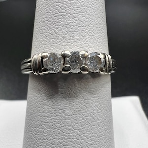 Op de afbeelding: Een zilveren ring met drie ronde, heldere edelstenen gezet in een band.