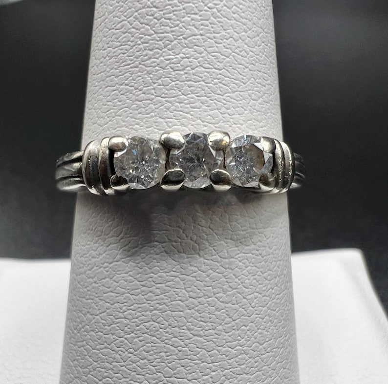 Op de afbeelding: Een zilveren ring met drie ronde, heldere edelstenen gezet in een band.