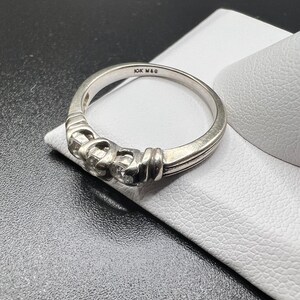 Op de afbeelding: Een zilveren bandring met drie kleine diamanten gezet in een decoratief ontwerp. De ring is gemarkeerd met "10K MAG" aan de binnenkant.