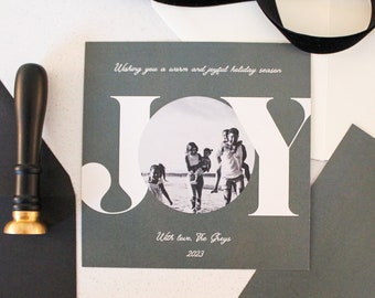 May include: A gray holiday card with the word "JOY" in white letters. A family photo is in the center of the word "JOY". The text "Wishing you a warm and joyful holiday season" is at the top of the card. The text "With love, The Groys 2022" is at the bottom of the card.