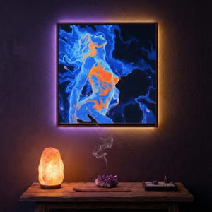 May include: A framed artwork featuring a blue and orange abstract figure against a dark backdrop. The artwork is lit by a warm light, with a purple and orange LED border. A Himalayan salt lamp and incense are on a wooden table, creating a relaxing atmosphere.