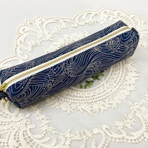May include: A navy blue pencil case with a gold and white wave pattern. The rectangular case has a gold zipper and a white border. The pencil case is approximately 8 inches long.