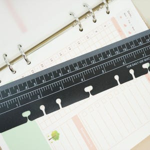 May include: Black ruler with white markings, measuring up to 8 inches, and the word "TODAY" printed on the left side. The ruler is designed to be a page finder and has the text "FOR DAILY USE QUICK PAGE FINDER". It is placed over a planner.