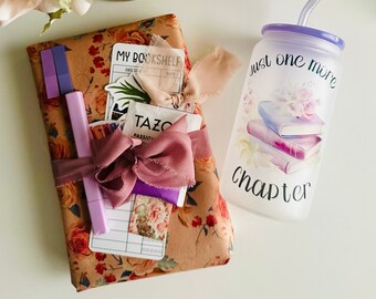 May include: A gift wrapped in floral patterned paper with a pink ribbon and a purple pen. A clear glass water bottle with a purple lid and straw has the text "just one more chapter" printed on it.
