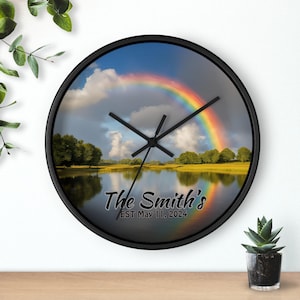 May include: Black round clock with a picture of a rainbow over a lake and trees. The text "The Smith's EST May 11, 2024" is printed on the clock face.