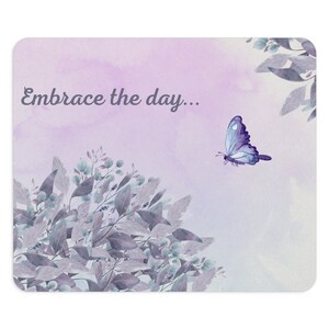 May include: A watercolor illustration of a purple butterfly flying over a cluster of light blue and purple leaves with the text "Embrace the day..." on a light purple background.