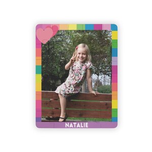 May include: A rectangular jigsaw puzzle featuring a photograph of a child sitting on a wooden bench, wearing a floral dress. The puzzle border is decorated with colorful squares and pink hearts, with the name NATALIE printed in white at the bottom.