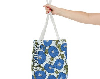 Puede incluir: Una bolsa de tela blanca con un estampado floral azul y la palabra "Sarah" impresa verticalmente en el lateral. La bolsa tiene una correa blanca.