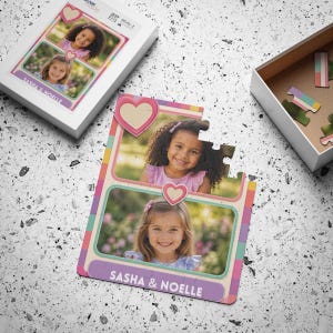 May include: A custom jigsaw puzzle featuring two rectangular photo frames with pink heart accents. The puzzle displays portraits of two young children and the text "SASHA & NOELLE" printed in white on a purple banner at the bottom of the puzzle.