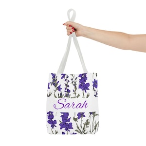 Peut inclure: Sac fourre-tout blanc avec un motif floral violet et le nom "Sarah" imprimé en violet sur le devant.