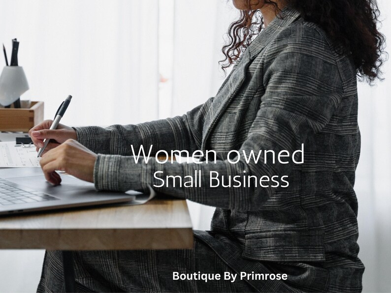 May include: A grey and black plaid blazer worn over a matching plaid skirt. The text "Women owned Small Business" is centered in white, with "Boutique By Primrose" at the bottom. A laptop and a pen are visible on a wooden desk surface.