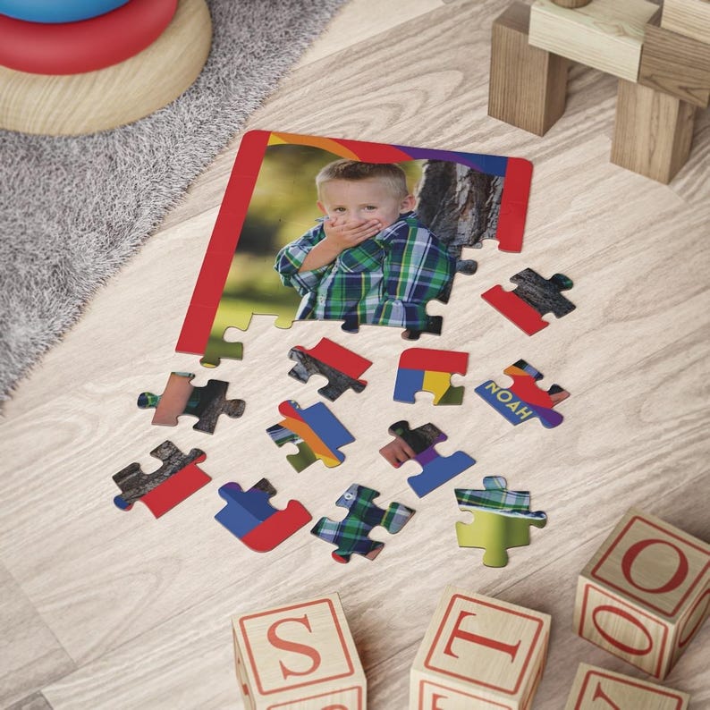 May include: A custom jigsaw puzzle featuring a photograph of a young child wearing a green and blue plaid shirt with their hands over their mouth. The puzzle is partially assembled with several loose pieces scattered below, one of which displays the name Noah.