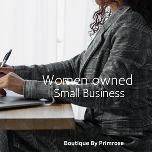 May include: A person wearing a grey and black plaid blazer and matching trousers, sitting at a wooden desk with a laptop and pen. The text "Women owned Small Business" and "Boutique By Primrose" is overlaid on the image in white lettering.