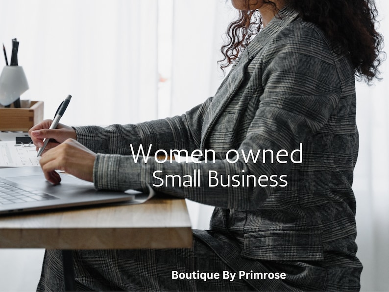 May include: A person wearing a grey and black plaid blazer and matching trousers, sitting at a wooden desk with a laptop and pen. The text "Women owned Small Business" and "Boutique By Primrose" is overlaid on the image in white lettering.