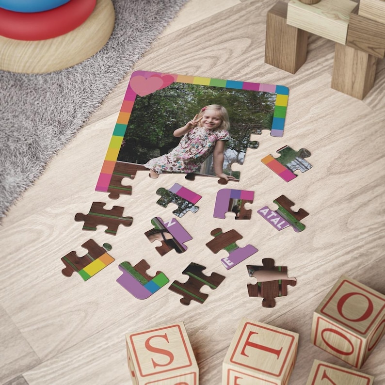 May include: A custom jigsaw puzzle featuring a photograph of a young child in a floral dress making a peace sign. The puzzle has a colorful border with a pink heart at the top and several detached puzzle pieces scattered below the main frame.