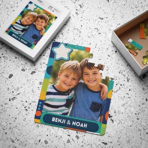 May include: A custom jigsaw puzzle featuring a photograph of two young boys, Benji and Noah, with a colorful border and a star icon. The puzzle is partially assembled, with the box lid showing the same image and the text Benji & Noah printed below.