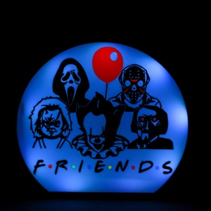 May include: A blue round light-up sign with a black silhouette of five horror movie characters, including Pennywise, Jason Voorhees, Freddy Krueger, Ghostface, and Chucky. The sign says "FRIENDS" in black letters with a red balloon above the characters.