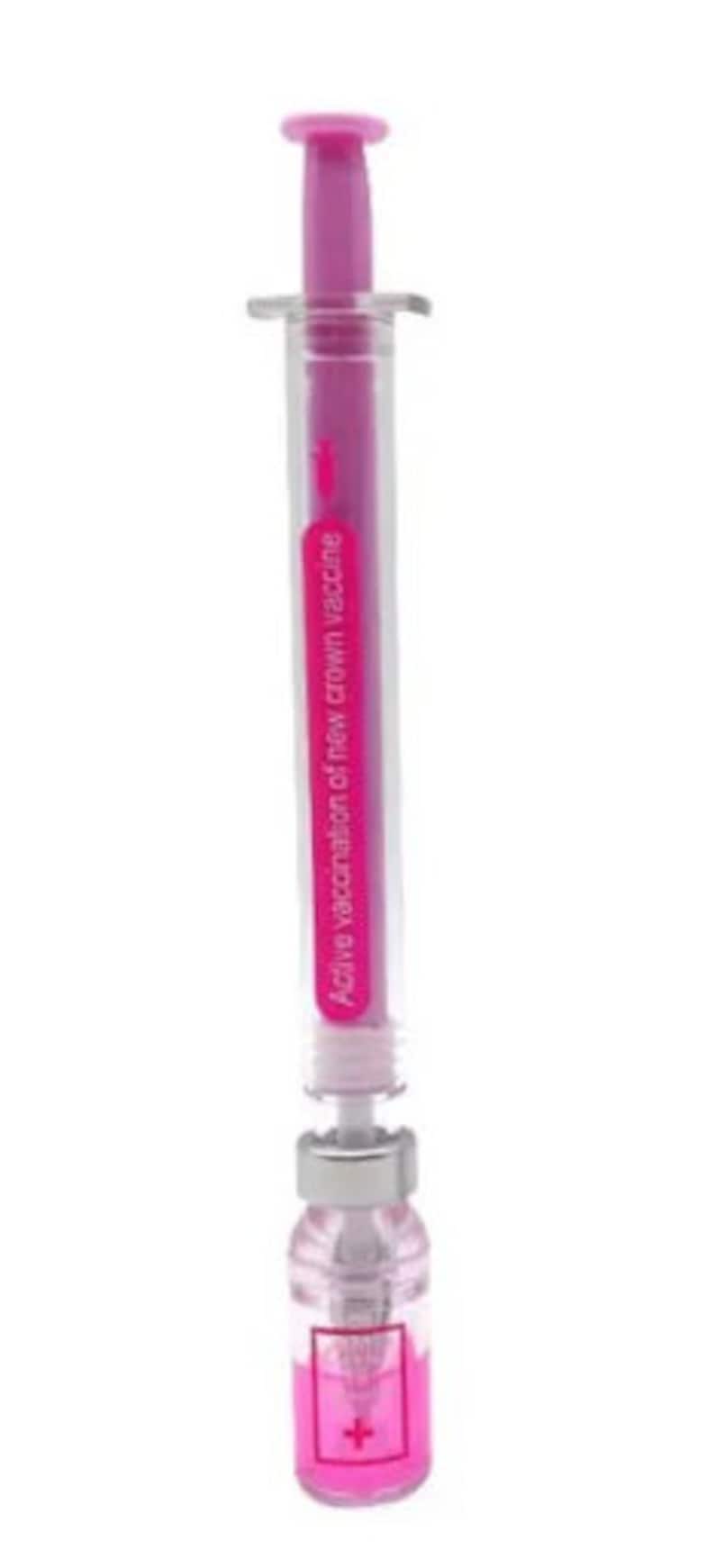 May include: A clear plastic syringe with a pink plunger and a pink liquid inside. The syringe has the text "Active vaccination of new crown vaccine" printed on it. A small bottle is attached to the syringe, also containing pink liquid.