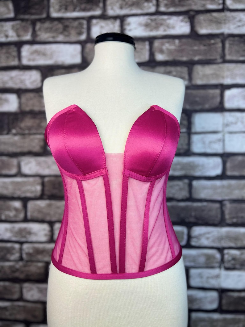 May include: A pink satin and mesh corset with a sweetheart neckline. The corset has boning and a hook and eye closure in the back.