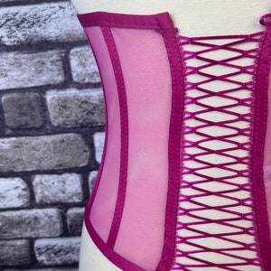 May include: A magenta mesh corset with satin ribbon lacing in the back. The corset has a satin trim and is designed to cinch the waist.