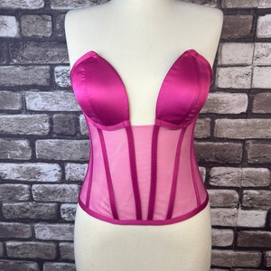 May include: A pink satin and mesh corset with a sweetheart neckline. The corset has boning and a hook and eye closure in the back.