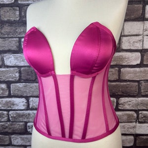 May include: A pink satin and mesh corset with a plunging neckline and boning. The corset has a sweetheart neckline and is strapless.