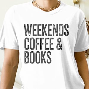May include: White t-shirt featuring the text "WEEKENDS COFFEE & BOOKS" in a distressed, dark grey font. The shirt has short sleeves and a crew neck. A gold chain necklace is visible.