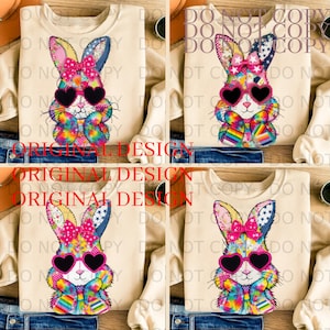 Può includere: Felpa beige con un design a coniglio patchwork colorato. Il coniglio indossa occhiali da sole a forma di cuore e un fiocco rosa. Il design include accenti arcobaleno e il testo "ORIGINAL DESIGN".