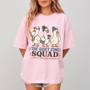 May include: Pink t-shirt featuring a graphic of three cartoon geese, each wearing accessories like a hat and glasses. The text "THE QUIET ZONE SQUAD" and "Off To Actively Monitor" are printed below the geese.