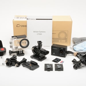 May include: A Crosstour CT9000 action camera set including a black camera, a waterproof housing, a remote control with a wrist strap, two batteries, a user manual, various black plastic mounting brackets, a memory card, and a cleaning cloth.