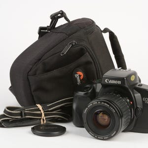 May include: A black Canon EOS 750 camera with a lens, lens cap, and a black camera bag. The camera bag has a shoulder strap and a Lowepro logo. The camera strap is black and gray.