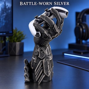 May include: A black and silver battle-worn gauntlet-shaped controller stand holding a white and black game controller. The text BATTLE-WORN SILVER is displayed above the object, which features mechanical plating and articulated finger details.