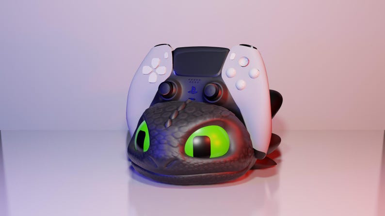 Pode incluir: Uma cabe&ccedil;a de drag&atilde;o preta e cinza com olhos verdes brilhantes suporta um controle PlayStation 5 branco e preto. O controle tem bot&otilde;es brancos e uma se&ccedil;&atilde;o central preta. A cabe&ccedil;a do drag&atilde;o tem uma superf&iacute;cie texturizada.