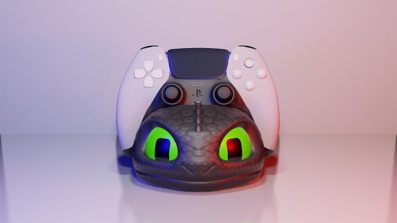 Pode incluir: Um suporte para comando PlayStation 5 com tema de drag&atilde;o preto e cinza. O suporte apresenta um design de cabe&ccedil;a de drag&atilde;o com olhos verdes brilhantes e um comando branco. O comando tem bot&otilde;es brancos e um centro preto.