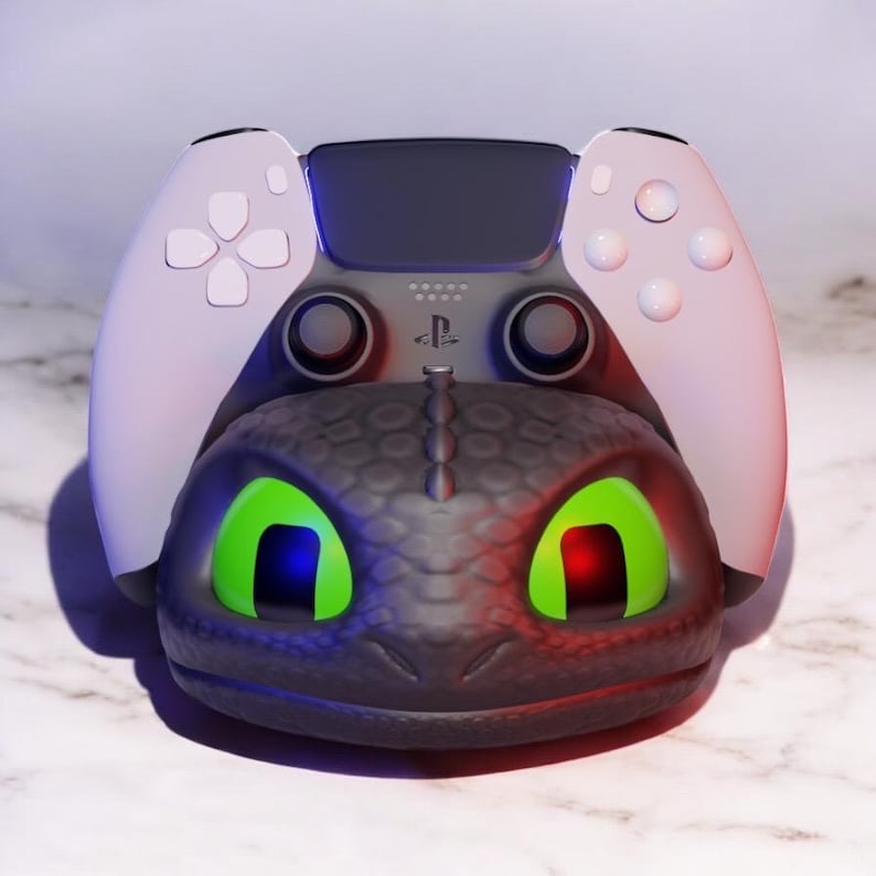 Pode incluir: Esta&ccedil;&atilde;o de carregamento de comando PlayStation 5 com tema de drag&atilde;o, em preto e cinza. Os olhos do drag&atilde;o brilham em verde com detalhes vermelhos e azuis. O comando &eacute; branco e cinza.